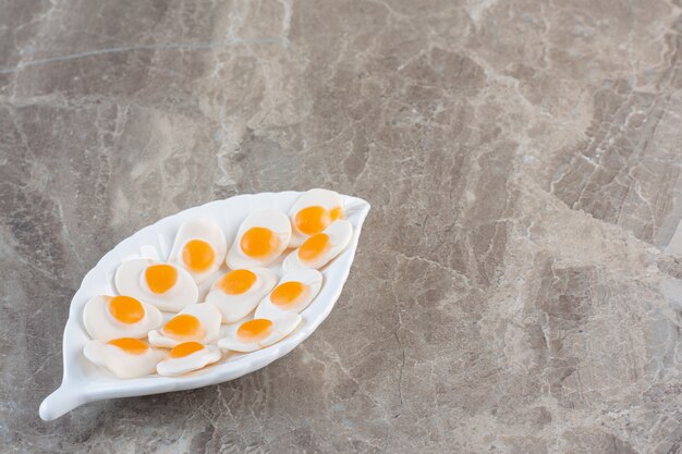 Candies in egg shape on white plate over grey background.