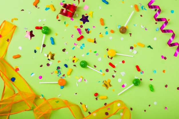 Candies and lollipops with confetti and curled streamer on green background