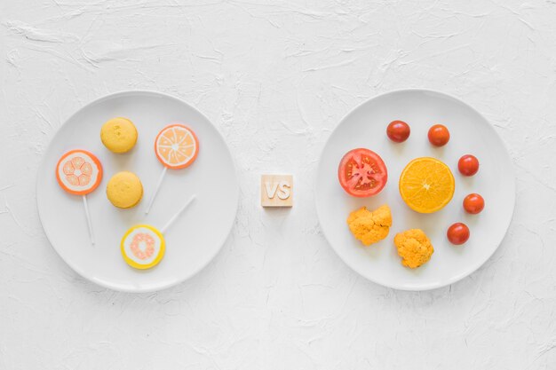 Candies versus healthy vegetable on white plate over textured background