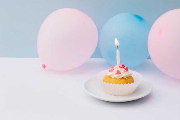 Candle on cupcake over plate with pink and blue balloons