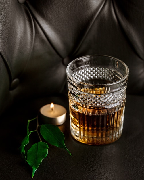 Free photo a candle, leaves and glass of whiskey