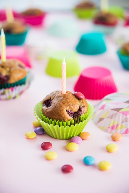 Candle on muffin with colorful candies on pink background