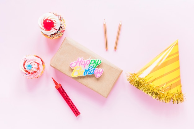 Candles and hat near cupcakes and present