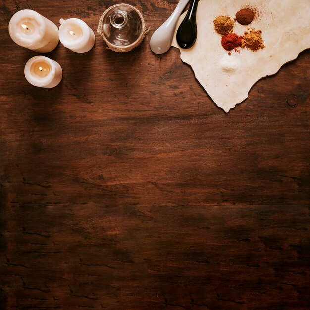 Candles near bottle and ingredients on parchment