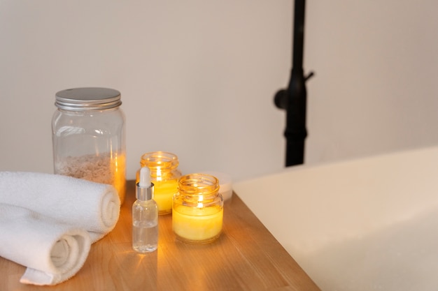 Candles, towels, bath salt, serum next to a bathtub filled with water