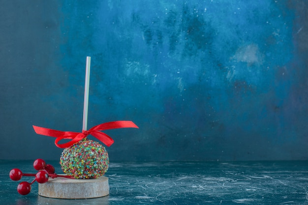 A candy coated lollipop and Christmas berry ornament on a piece of wood on blue background. High quality photo