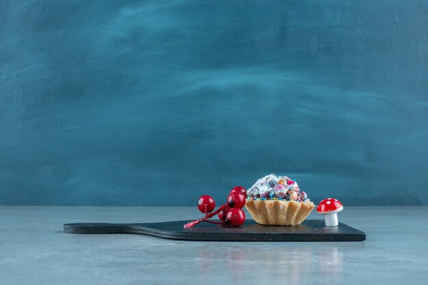 Candy topped cupcake and christmas ornaments on a black board on marble surface