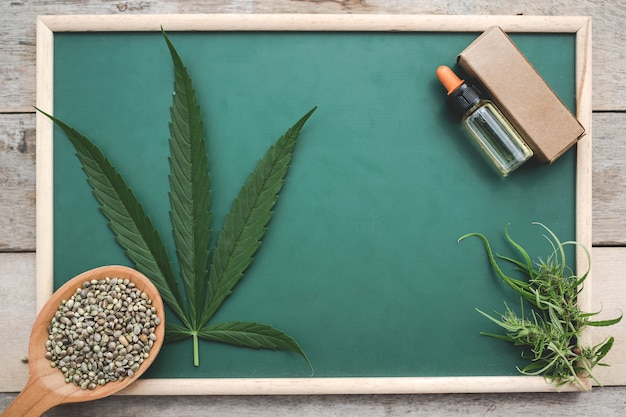 Cannabis, cannabis seeds, cannabis leaves, cannabis oil placed on a green board on a wooden floor.