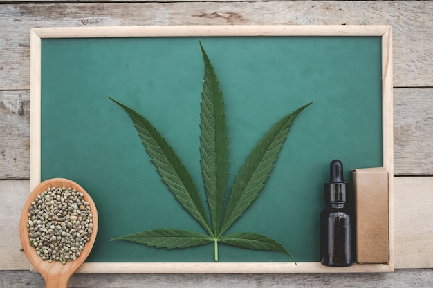 Foto gratuita cannabis, semi di cannabis, foglie di cannabis, olio di cannabis posizionato su una tavola verde su un pavimento di legno.