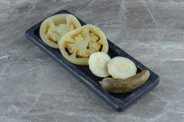 Canned green tomato and cucumber on wooden plate.