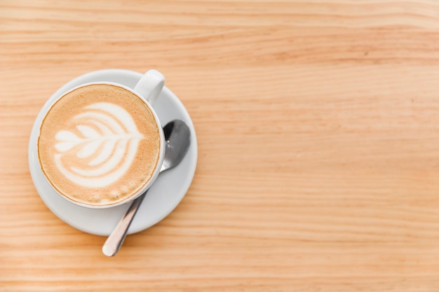 Cappuccino coffee with art latte and spoon on wooden background