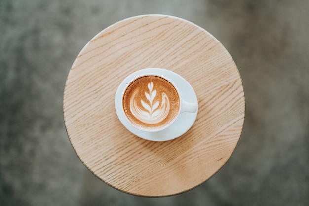 Foto gratuita cappuccino su una tazza di ceramica bianca con un piattino sul tavolo rotondo marrone