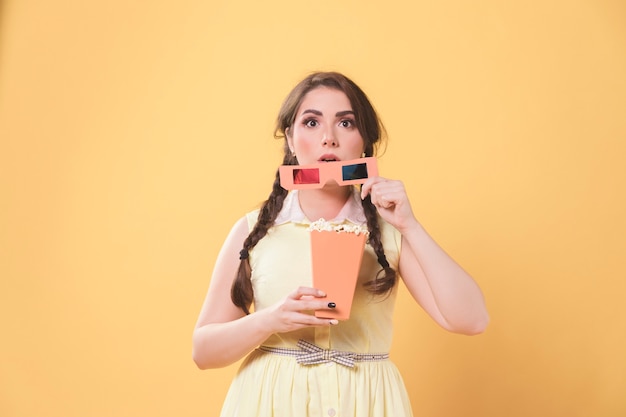 Captivated woman holding up movie glasses and popcorn