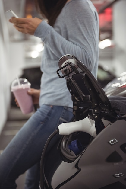 女性が立っている間に電気自動車の充電器で充電されている車