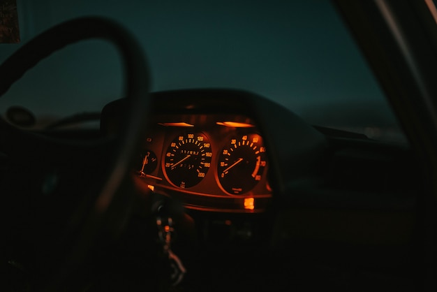 Car dashboard lit in red with a steering wheel at night