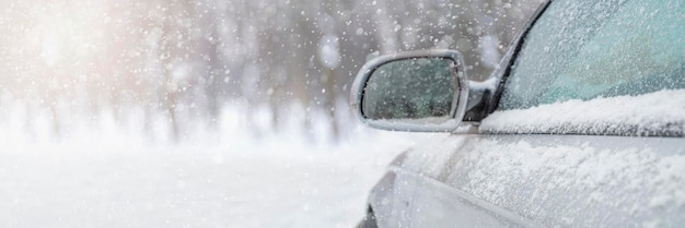 The car drives through the snow, the bright winter sun shines against the background of the forest. close-up rearview mirror. the vehicle is covered with snow. snowing.