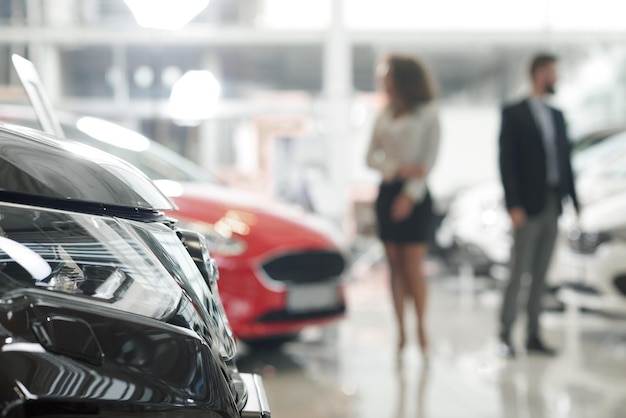 Free photo car headlight and people observing automobiles in showroom