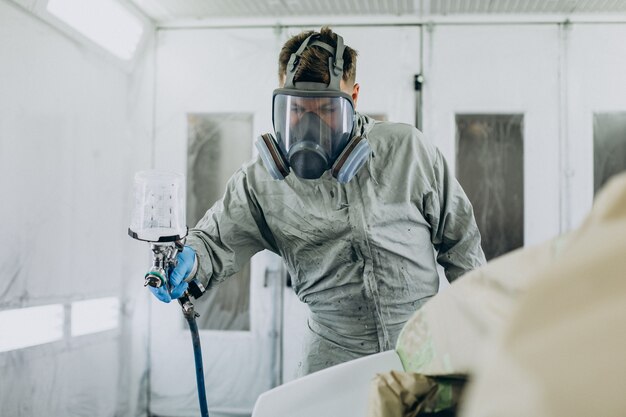 Car mechanic painting car with spray gun