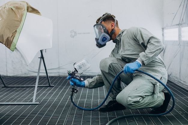 Car mechanic painting car with spray gun