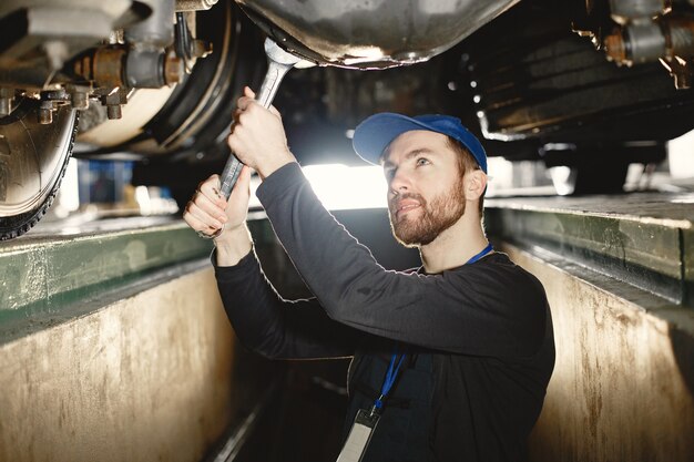 Car mechanic repairs blue car on rise in  garage