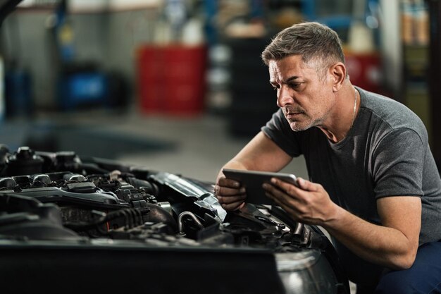 Car mechanic using digital tablet while repairing analyzing engine in auto repair shop