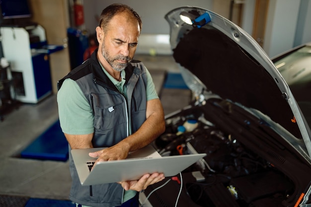 Foto gratuita meccanico di auto che utilizza il laptop durante l'esecuzione della diagnostica del motore in officina