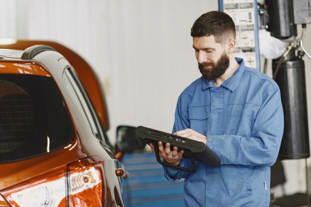 Car mechanic with a tablet near car in work clothes