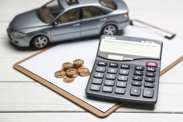 Модель автомобиля, калькулятор и монеты на белом столе