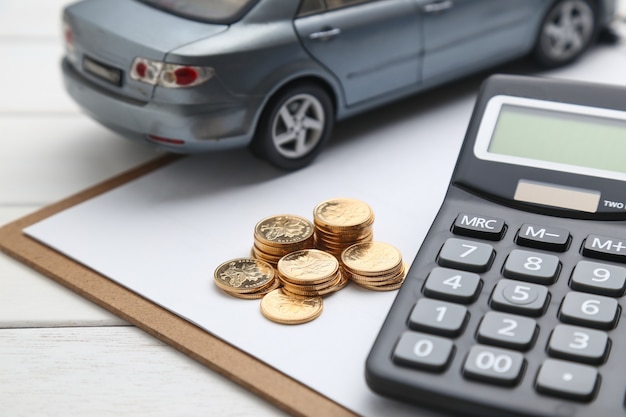 Modello di auto, calcolatrice e monete sul tavolo bianco