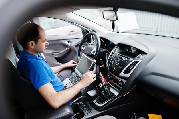 자동차 수리 및 유지 관리 테마 자동차 서비스에서 제복을 입은 전기 정비공이 노트북과 함께 obd 장치를 사용하여 자동차 진단을 하고 있습니다.
