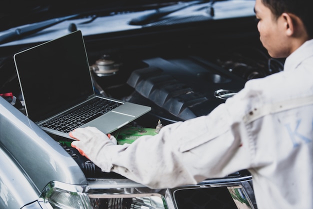 Free photo car repairman wearing a white uniform standing and holding a wrench that is an essential tool for a mechanic with laptop checking engine