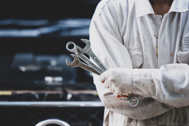 Car repairman wearing a white uniform standing and holding a wrench that is an essential tool for a mechanic