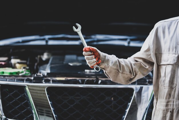 Car repairman wearing a white uniform standing and holding a wrench that is an essential tool for a mechanic