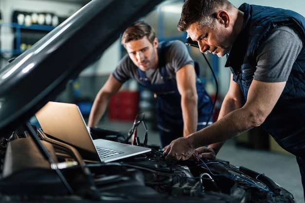 Car repairmen using laptop while doing car engine diagnostic in auto repair shop