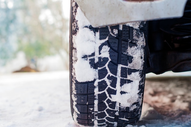 Автомобильные шины на зимней дороге покрыты снегом. Транспортное средство на заснеженной аллее утром при снегопаде