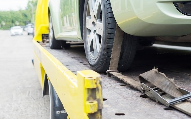 Foto gratuita camion di soccorso stradale durante il lavoro utilizzando la cintura bloccata per il trasporto di altre auto verdi