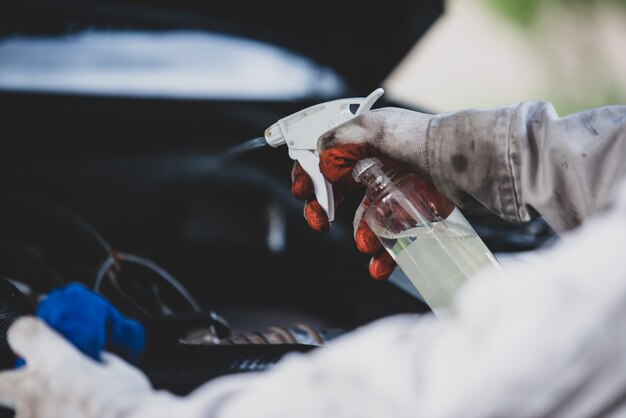 Работник мойки нося белую форму стоя губка для того чтобы очистить автомобиль в центре мойки, концепция для индустрии ухода за автомобилем.