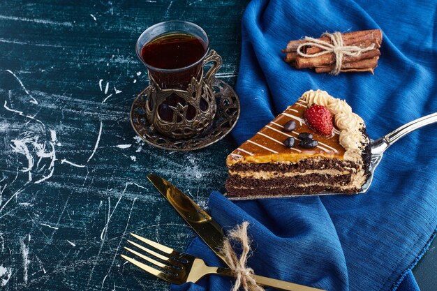 Кусочек карамельного торта на синей поверхности со стаканом чая.