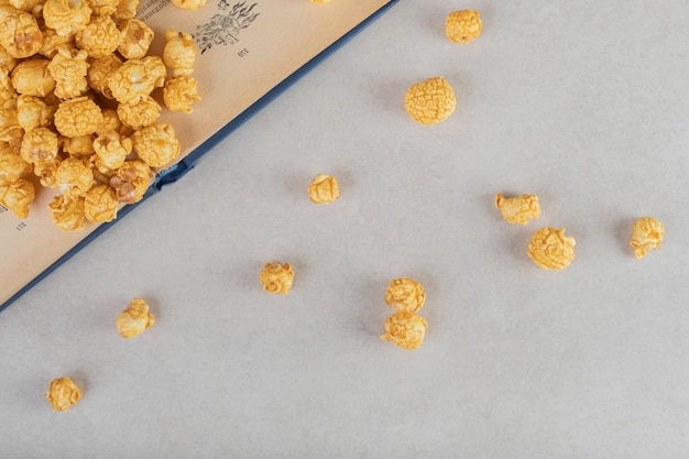 Free photo caramel coated popcorn scattered over and in front of an open book on marble background.