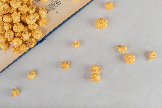 Caramel coated popcorn scattered over and in front of an open book on marble background.