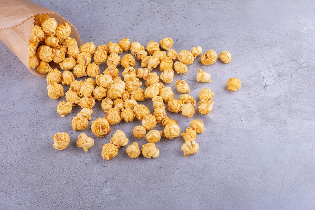Caramel flavored popcorn spilling out of paper wrapping on marble background. High quality photo