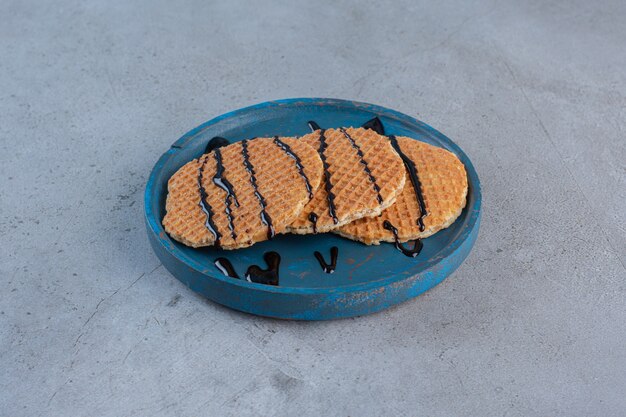 Caramel waffles decorated with chocolate sauce on blue plate.