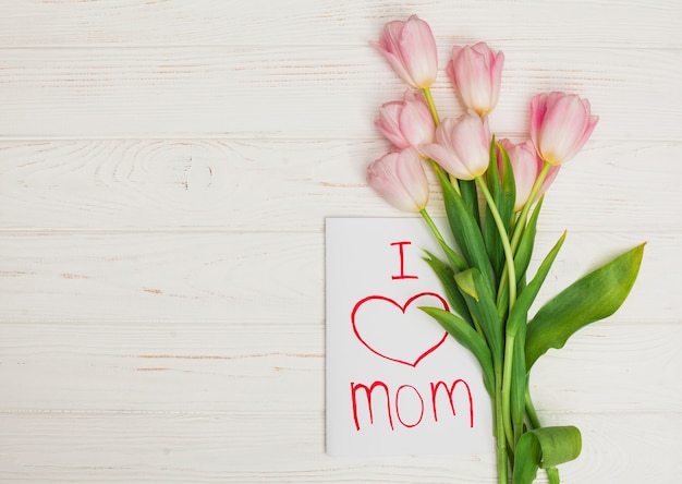 Card I love mom and flowers placed on white wood table 