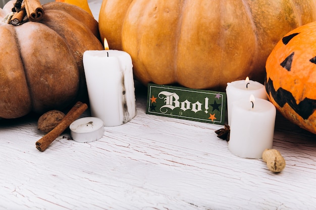 Card with lettering 'Boo' stands before scarry Halloween pumpkins