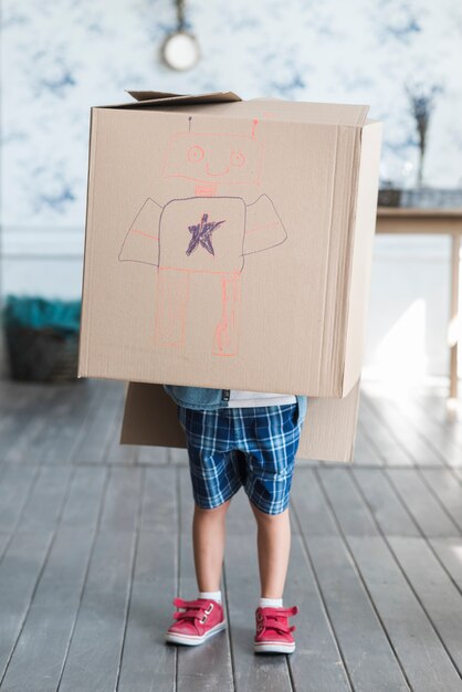 Cardboard box drawn with robot over the boy standing in the room