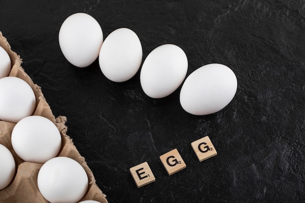 Scatola delle uova di cartone con uova di gallina bianche su un tavolo nero.