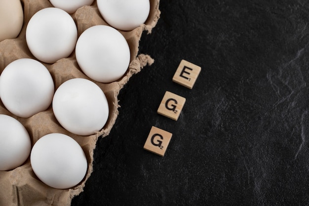 Free photo cardboard egg box with white chicken eggs on a black table.