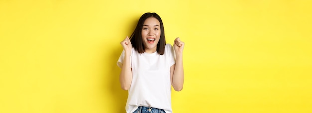 Free photo carefree asian girl dancing and having fun posing in white tshirt against yellow background