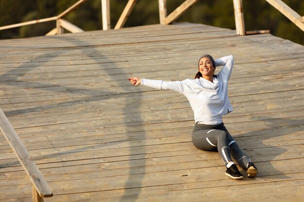 Carefree athletic woman with eyes closed enjoying in morning time while relaxing on wooden bridge Copy space