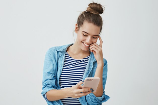 Carefree attractive young european woman smiling happily holding smartphone looking display